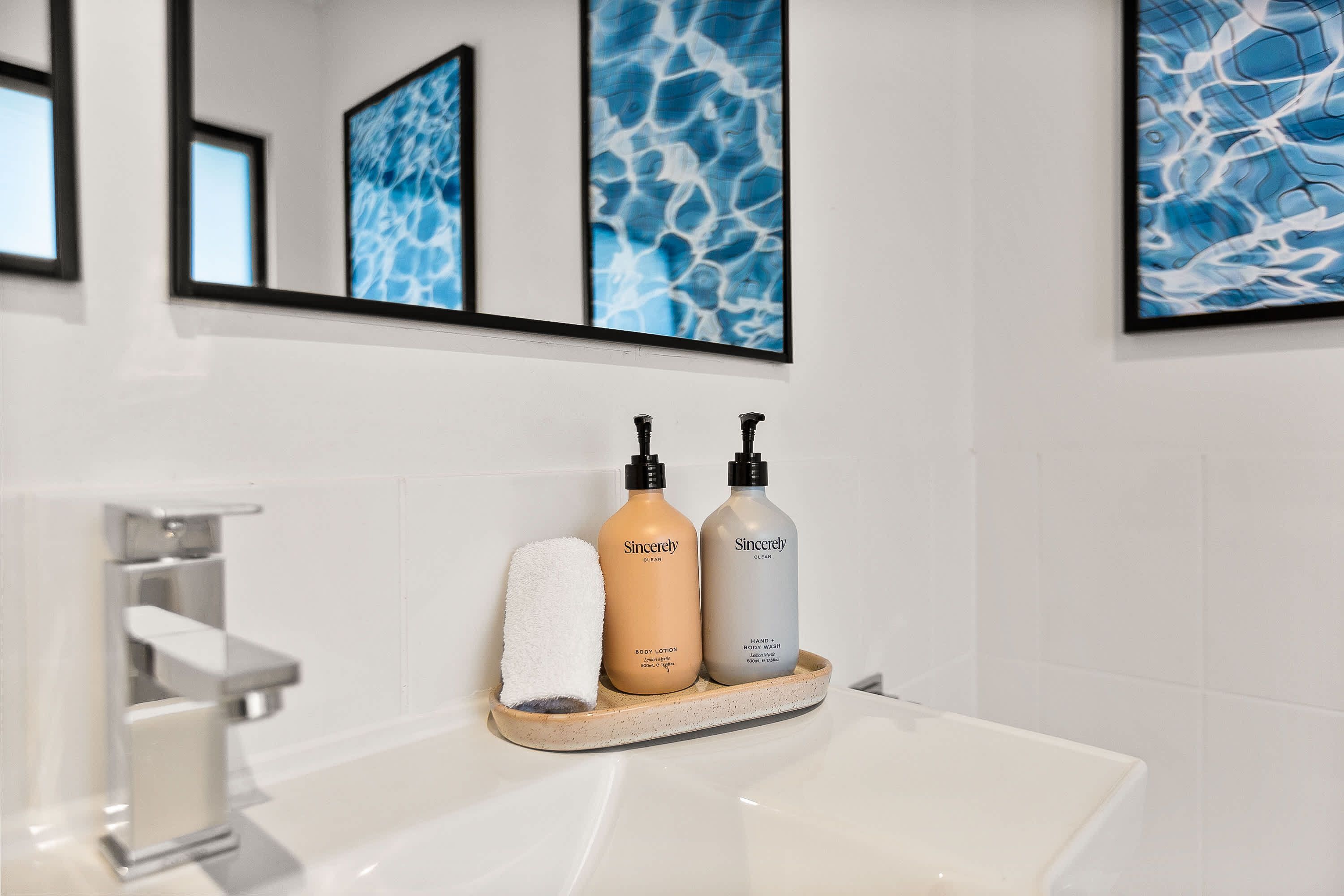 A bathroom with a white sink, two bottles of body lotion, and a white towel on a tray.