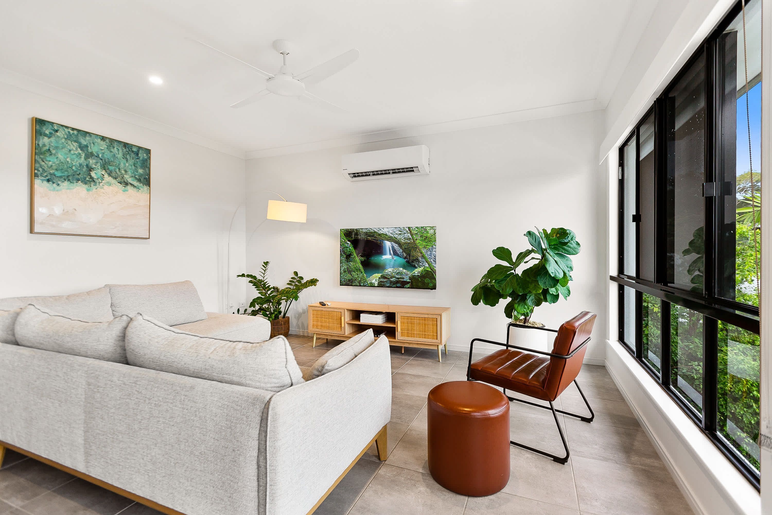 A modern living room with a sofa, a coffee table, a TV, and large windows.