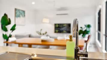 A modern kitchen with a stainless steel sink, a wooden dining table, and a green bottle on the counter.