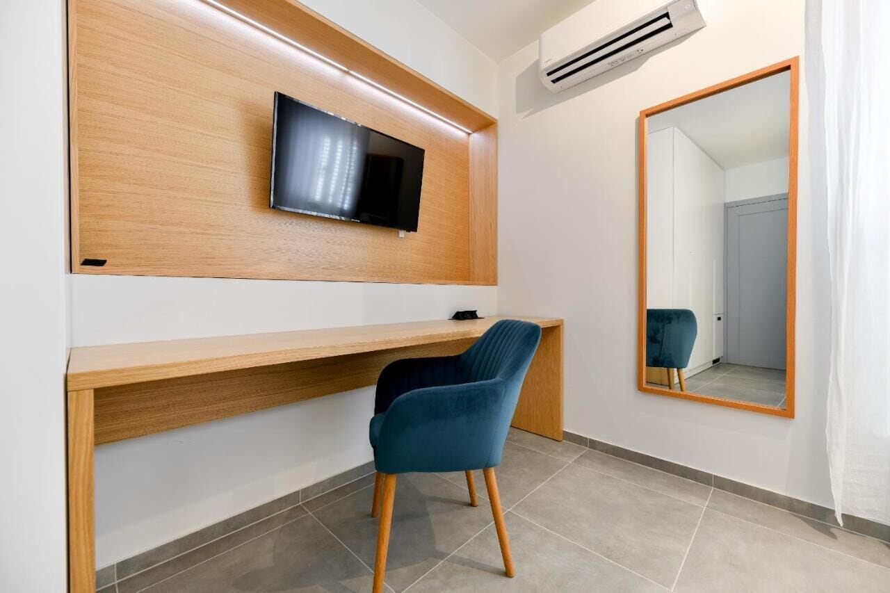 A modern room with a wooden desk, a blue chair, a mounted TV, and a large mirror.