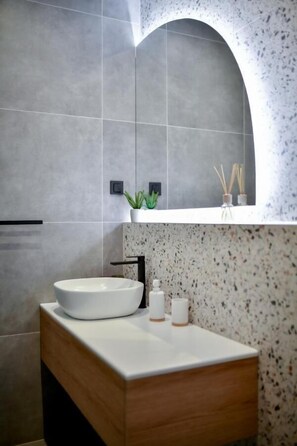 A modern bathroom with a freestanding white sink, a wooden vanity, and a speckled backsplash. - Maris Accommodation (Zadar)