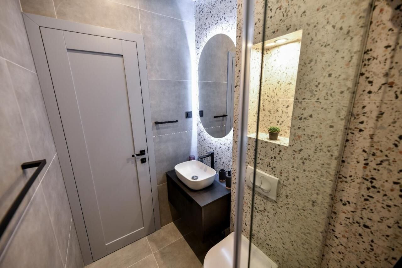 Un baño moderno con una puerta blanca, un lavamanos independiente y un espejo con luz.