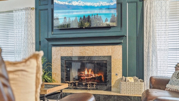 Ein Wohnzimmer mit Kamin, einem darüber hängenden Fernseher und Blick auf eine Berglandschaft.