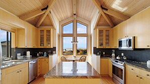 A modern kitchen with wooden cabinets, a central island, and a large window offering a view. - Amazing Oceanview's - Dog-Friendly 4BR with Sauna (Bodega Bay)