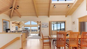 A spacious kitchen with wooden beams, a dining area with wooden chairs, and large windows offering views. - Amazing Oceanview's - Dog-Friendly 4BR with Sauna (Bodega Bay)