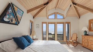 A bedroom with a large bed, a wooden ceiling, and a view through the windows. - Amazing Oceanview's - Dog-Friendly 4BR with Sauna (Bodega Bay)