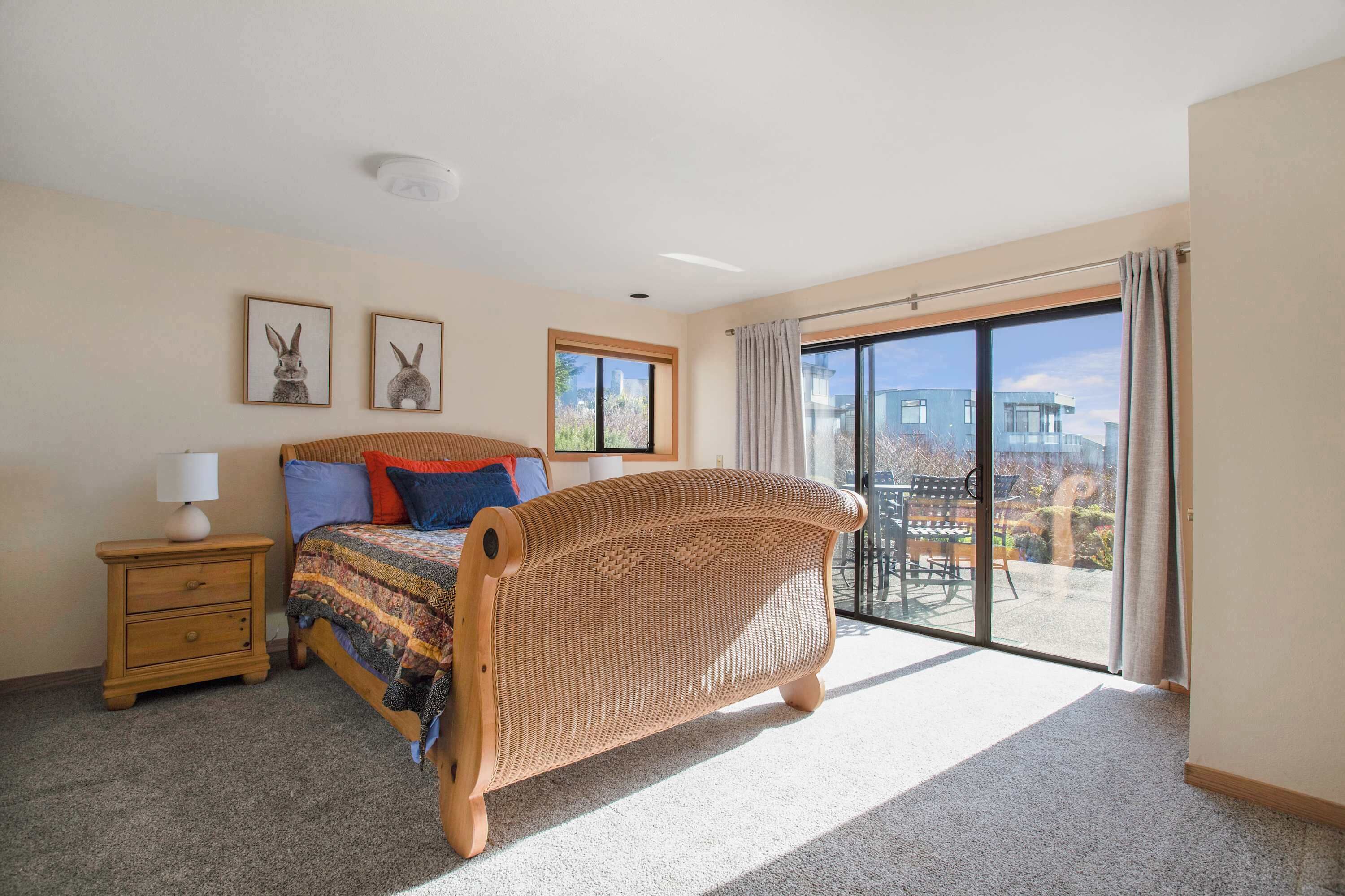 A bedroom with a large bed, a nightstand, two framed pictures, and a sliding glass door to an outdoor area.