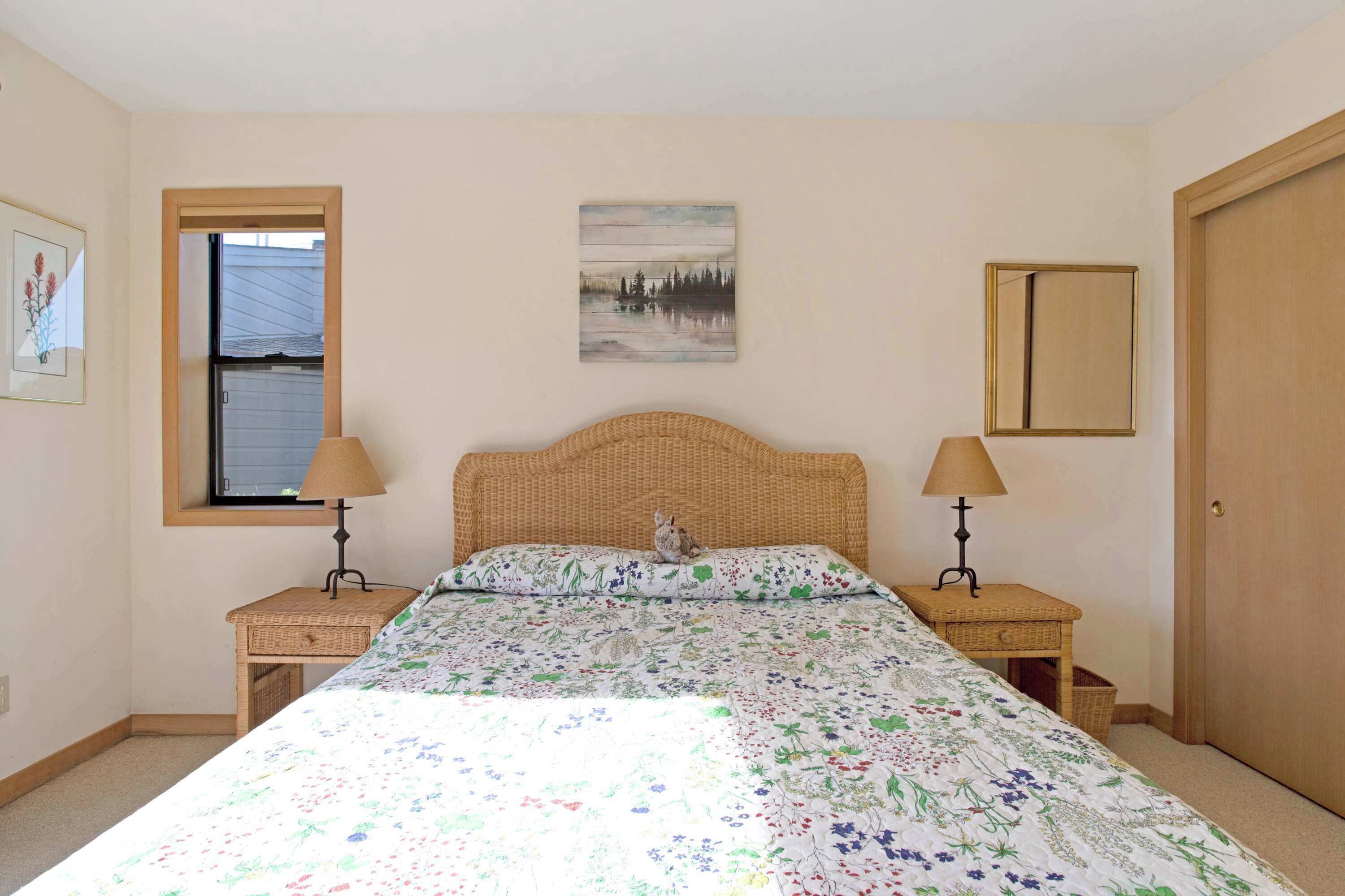 A bedroom with a bed, two nightstands, a window, a painting, and a door.