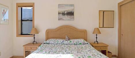 A bedroom with a bed, two nightstands, a window, a painting, and a door.