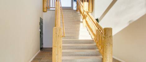 Una escalera con barandillas de madera y suelo de piedra que conduce a una puerta con paneles de vidrio.