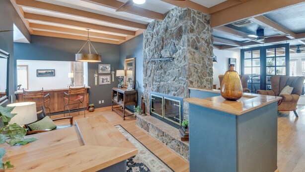 A spacious living area with a stone fireplace, wooden furniture, and a ceiling fan. - Game Room, Media Room & Pool: Luxe Villa in Craig! (Craig)