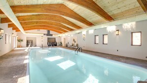 A large indoor swimming pool with wooden beams on the ceiling, a seating area with chairs and tables, and a potted plant. - Game Room, Media Room & Pool: Luxe Villa in Craig! (Craig)