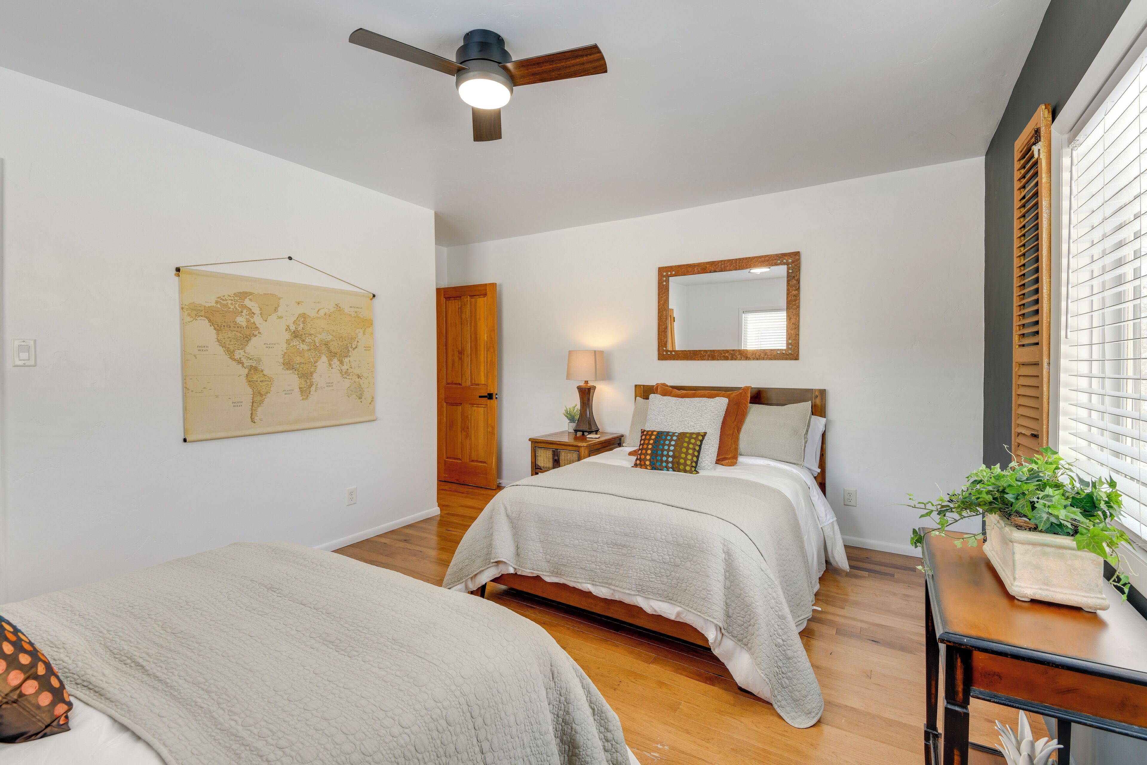 A bedroom with two beds, a ceiling fan, a world map, a mirror, and a window with blinds.