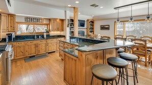 A spacious kitchen with wooden cabinets, a central island with stools, and a dining area with wooden chairs. - Game Room, Media Room & Pool: Luxe Villa in Craig! (Craig)