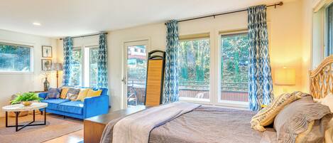 Un dormitorio con una cama grande, un sofá azul y vistas al exterior a través de las ventanas.