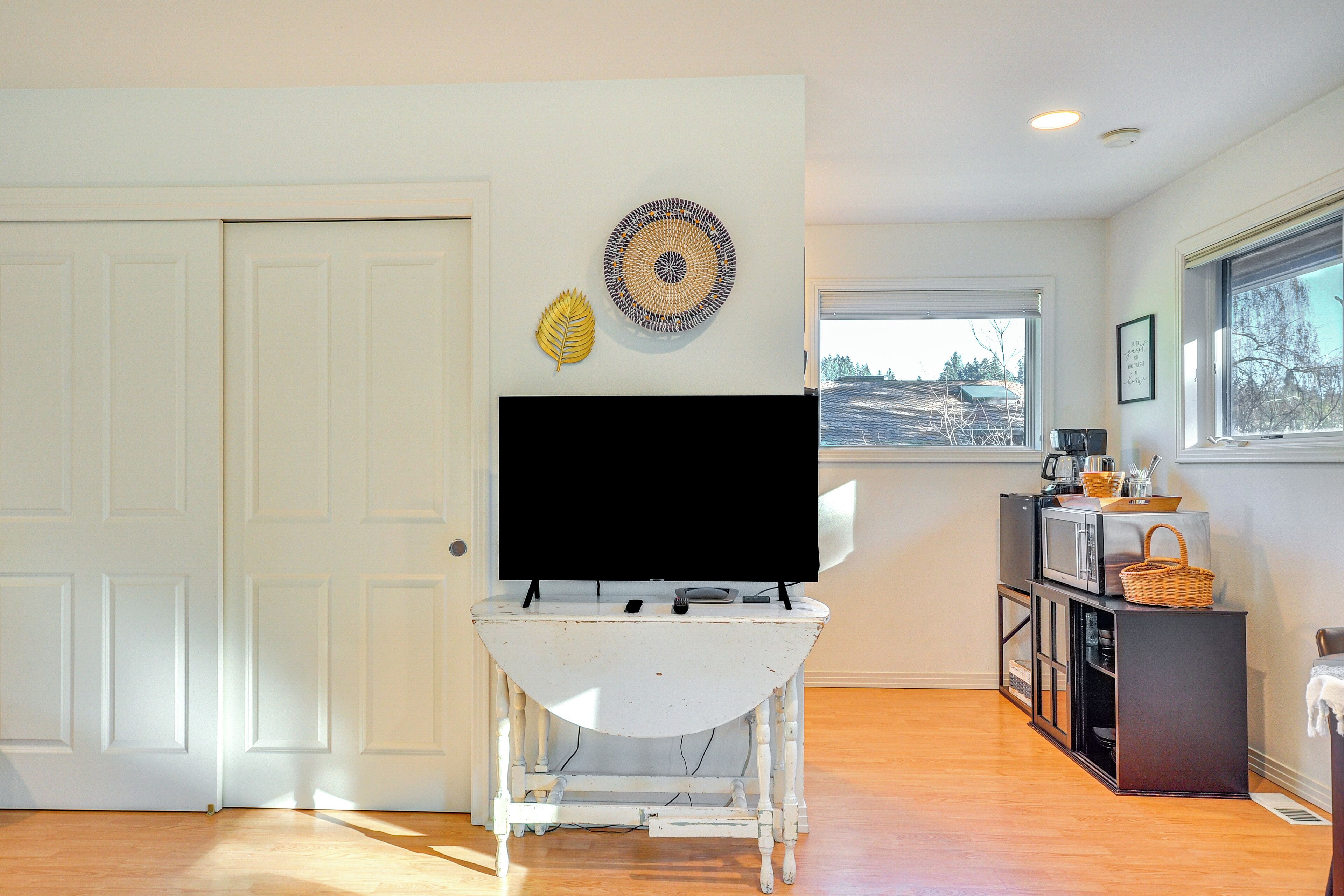 Una sala de estar con un mueble blanco para televisor, un televisor de pantalla plana, una hoja decorativa y una obra de arte circular en la pared.