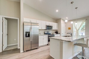 A modern kitchen with white cabinets, stainless steel appliances, and a marble countertop.