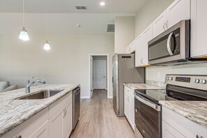 A modern kitchen with a stainless steel refrigerator, microwave, and oven, marble countertops, and pendant lighting. - 2 Mi to Rainbow Springs: Home w/ Hot Tub! (Dunnellon)