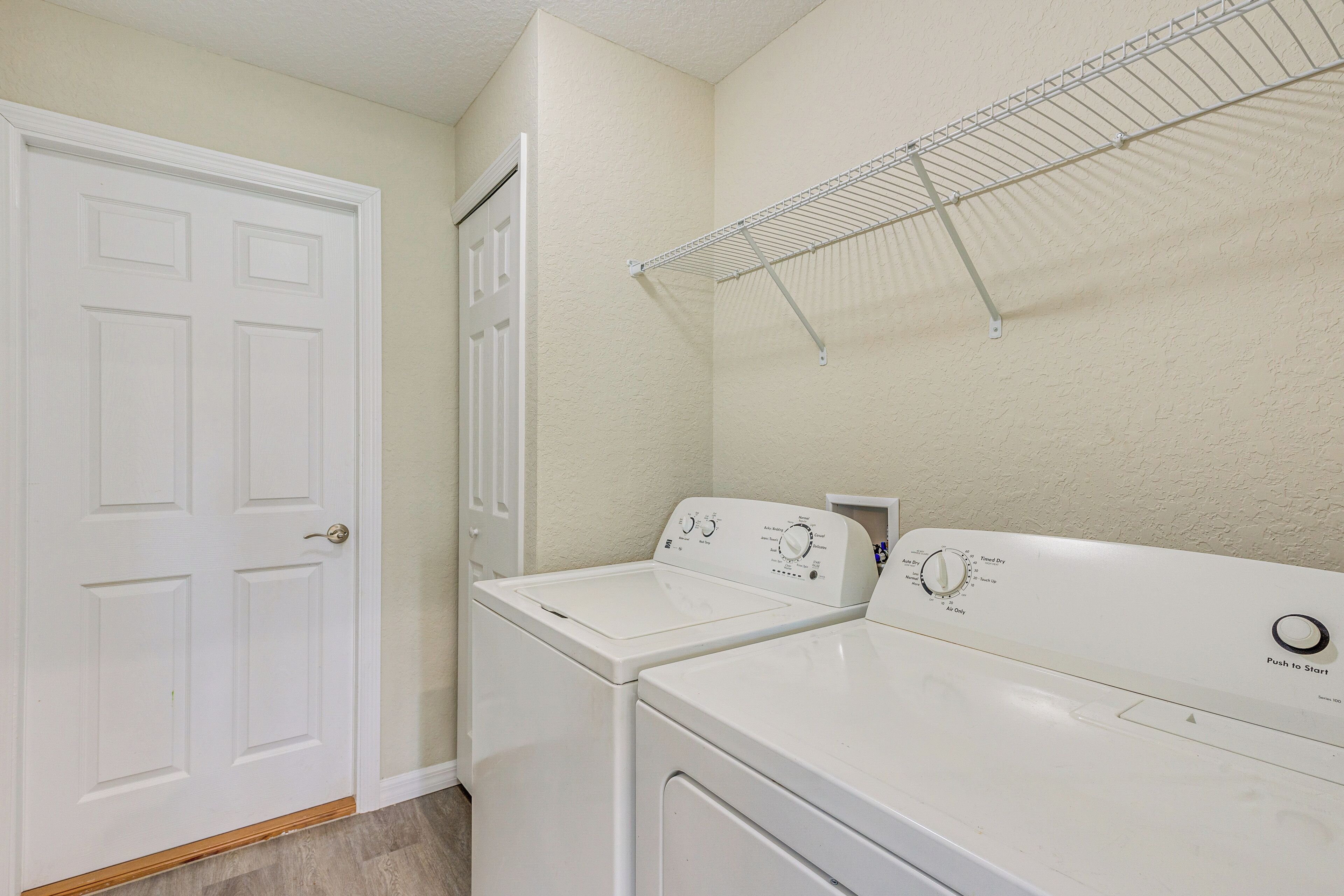 A laundry room with two white front-loading washers and dryers, a white door, and a metal drying rack on the wall.