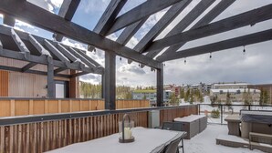 Eine Terrasse im Freien mit einem mit Schnee bedeckten Tisch und Stühlen, einem Holzzaun und Blick auf Gebäude im Hintergrund.