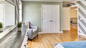 A room with a wooden floor, a gray upholstered chair, a white door, and a mirror with striped wallpaper.