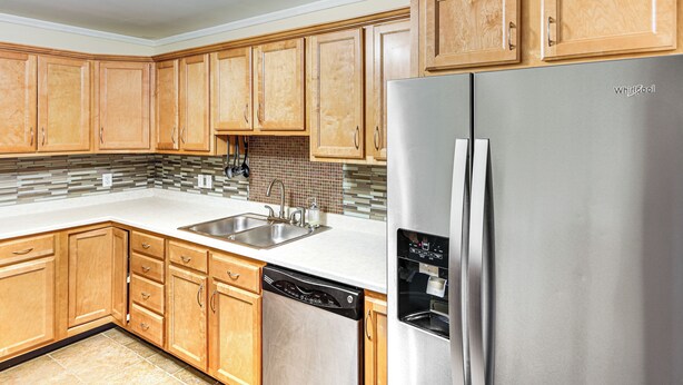 A modern kitchen with wooden cabinets, a stainless steel refrigerator, a dishwasher, and a tiled backsplash.