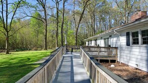 A wooden deck leading to a white house with a brick chimney, surrounded by trees. - Game Room! Serene 15-acre Nature Escape in Delmar (Delmar)