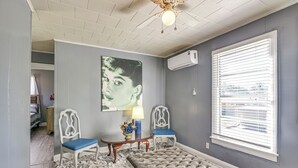 A room with a tufted ottoman, two chairs, a table with a lamp, a wall-mounted air conditioner, and a window with blinds. - Near Sabine Lake & Refineries: Pet-friendly Apt (Port Arthur)
