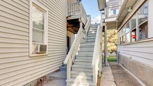 Un étroit escalier extérieur mène à un balcon situé au deuxième étage, lequel est agrémenté d’une rambarde en métal.