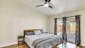 Een slaapkamer met een bed, nachtkastje, plafondventilator en een raam met gordijnen.