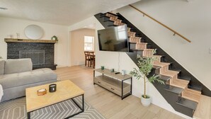 Una sala de estar moderna con sofá, mesa de centro y chimenea. Una escalera con un televisor montado en la pared conduce a otra habitación.