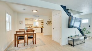 Un amplio salón con una mesa de comedor de madera, un televisor de pantalla plana montado en la pared y una escalera que conduce a otro nivel.