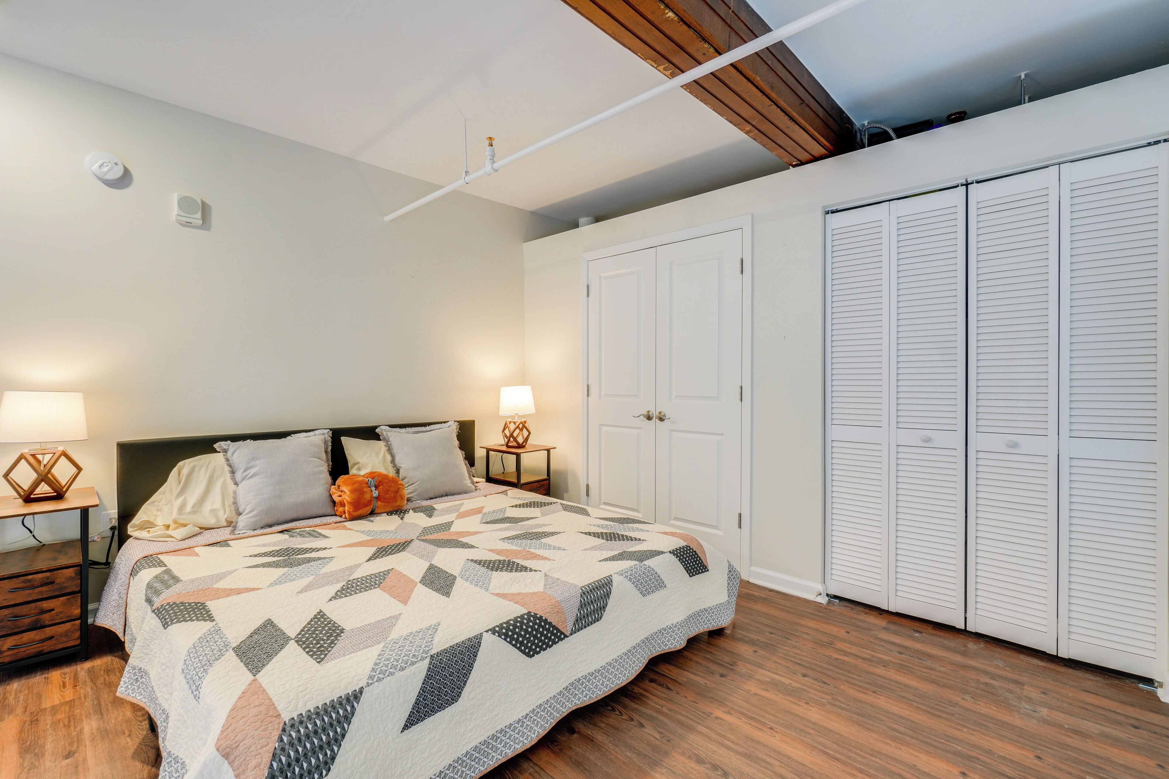 A bedroom with a bed, two bedside tables, a nightstand, a closet, and a ceiling with exposed beams.