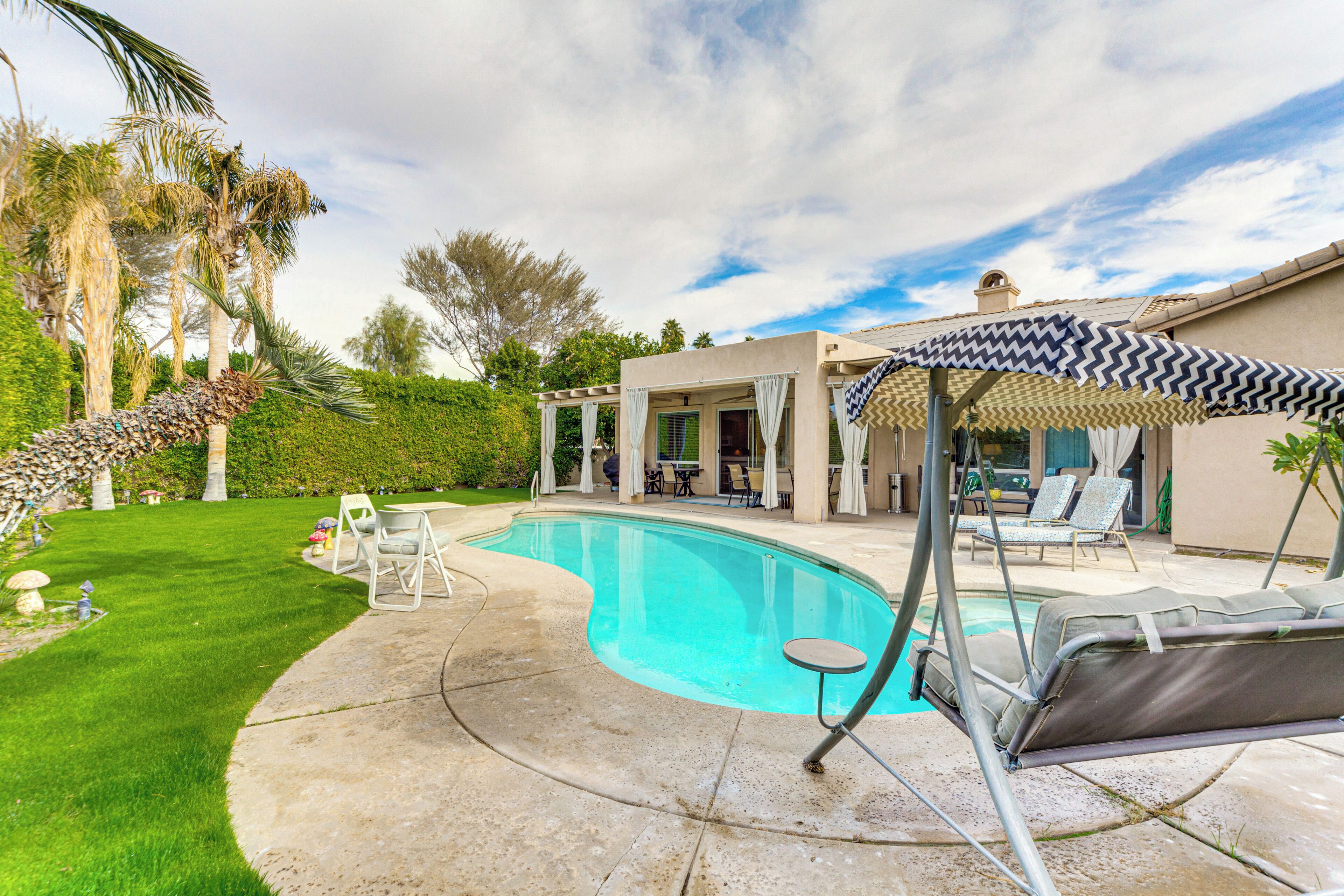 A swimming pool with lounge chairs and an umbrella, surrounded by a well-maintained lawn and palm trees.