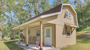 A single-story wooden house with a covered porch, a front door, and a small attached garage. - On 40 Acres: Charming Cabin in Zanesville! (Zanesville)