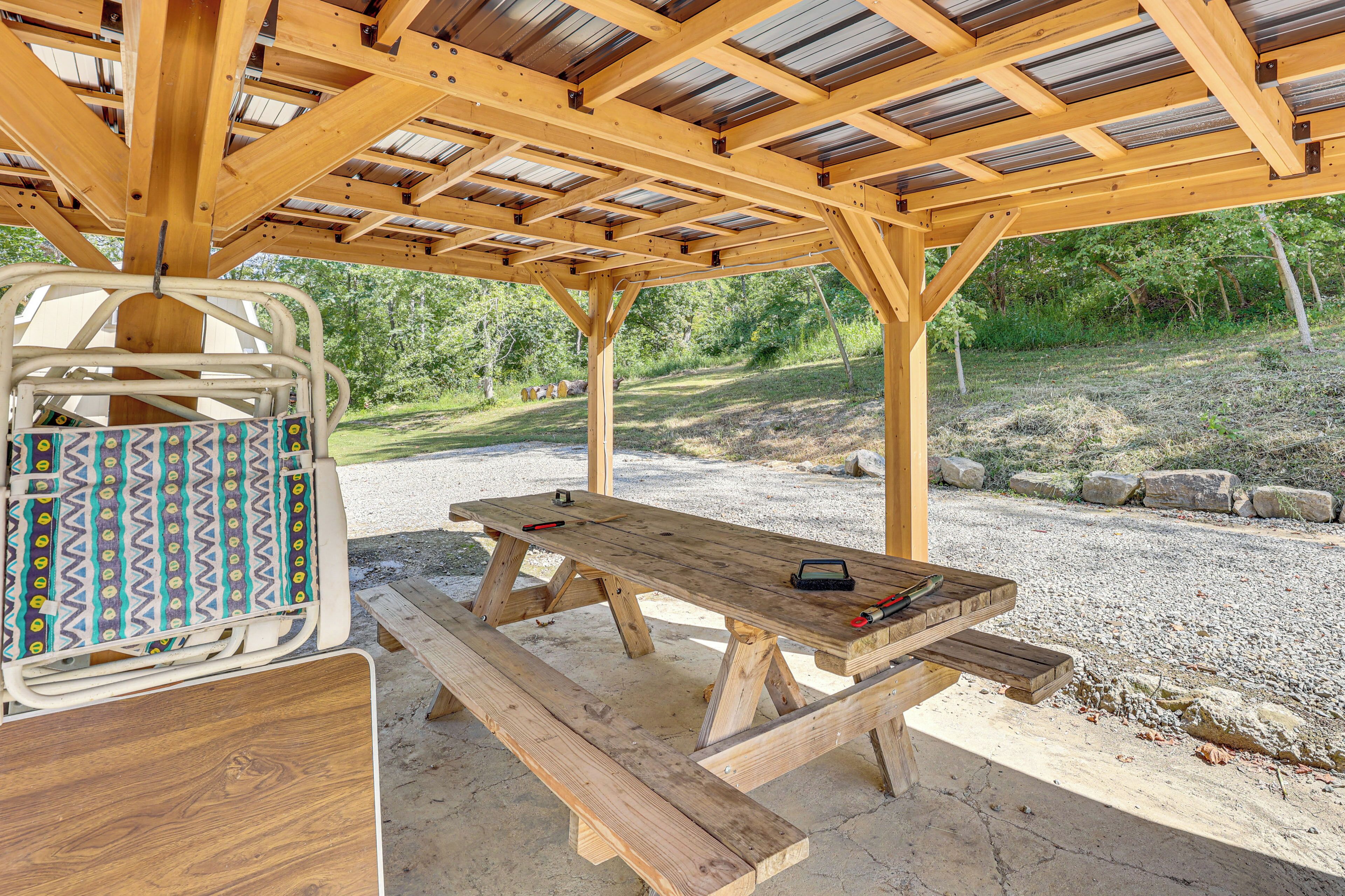A wooden picnic table with benches, a metal chair with a patterned cushion, and a metal grill on the table.