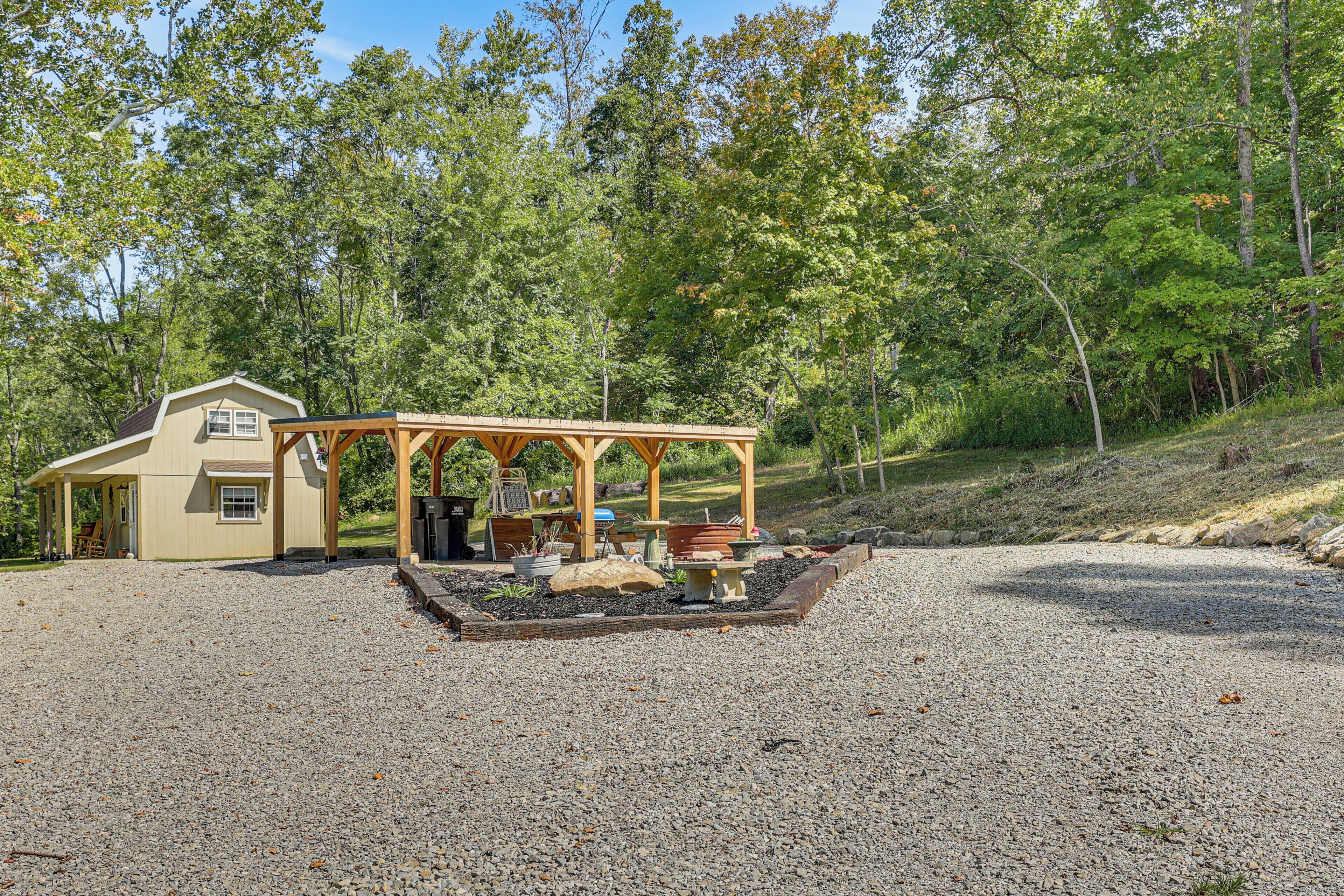 A house with a covered patio area, a gravel driveway, and a forested hillside in the background.