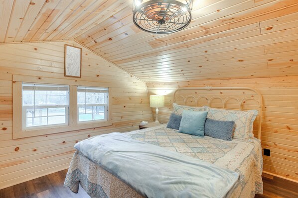 Un dormitorio rústico de cabaña de madera con cama, mesita de noche y ventilador de techo.