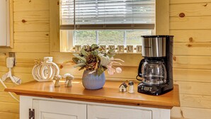 A wooden interior with a kitchen counter, a coffee maker, a vase with flowers, and a window with blinds. - On 40 Acres: Charming Cabin in Zanesville! (Zanesville)