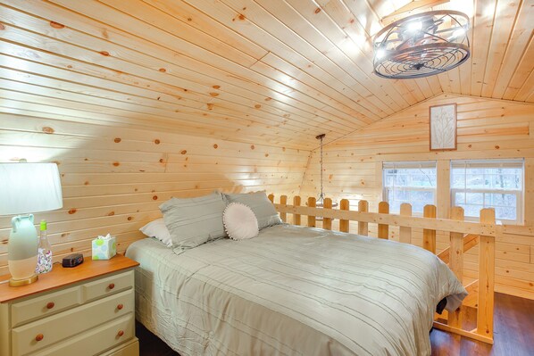 A cozy wooden cabin bedroom with a bed, bedside table, lamp, and a window with a view. - On 40 Acres: Charming Cabin in Zanesville! (Zanesville)