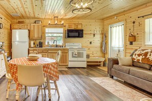 A cozy cabin interior with wooden walls, a dining area with a checkered tablecloth, a kitchenette with modern appliances, and a comfortable seating area with a leather couch. - On 40 Acres: Charming Cabin in Zanesville! (Zanesville)