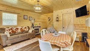 A cozy cabin interior with a wooden ceiling, a fireplace, a dining table with chairs, a sofa, and a television mounted on the wall. - On 40 Acres: Charming Cabin in Zanesville! (Zanesville)