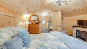 A cozy wooden cabin bedroom with a bed, dresser, mirror, and fireplace. - On 40 Acres: Charming Cabin in Zanesville! (Zanesville)