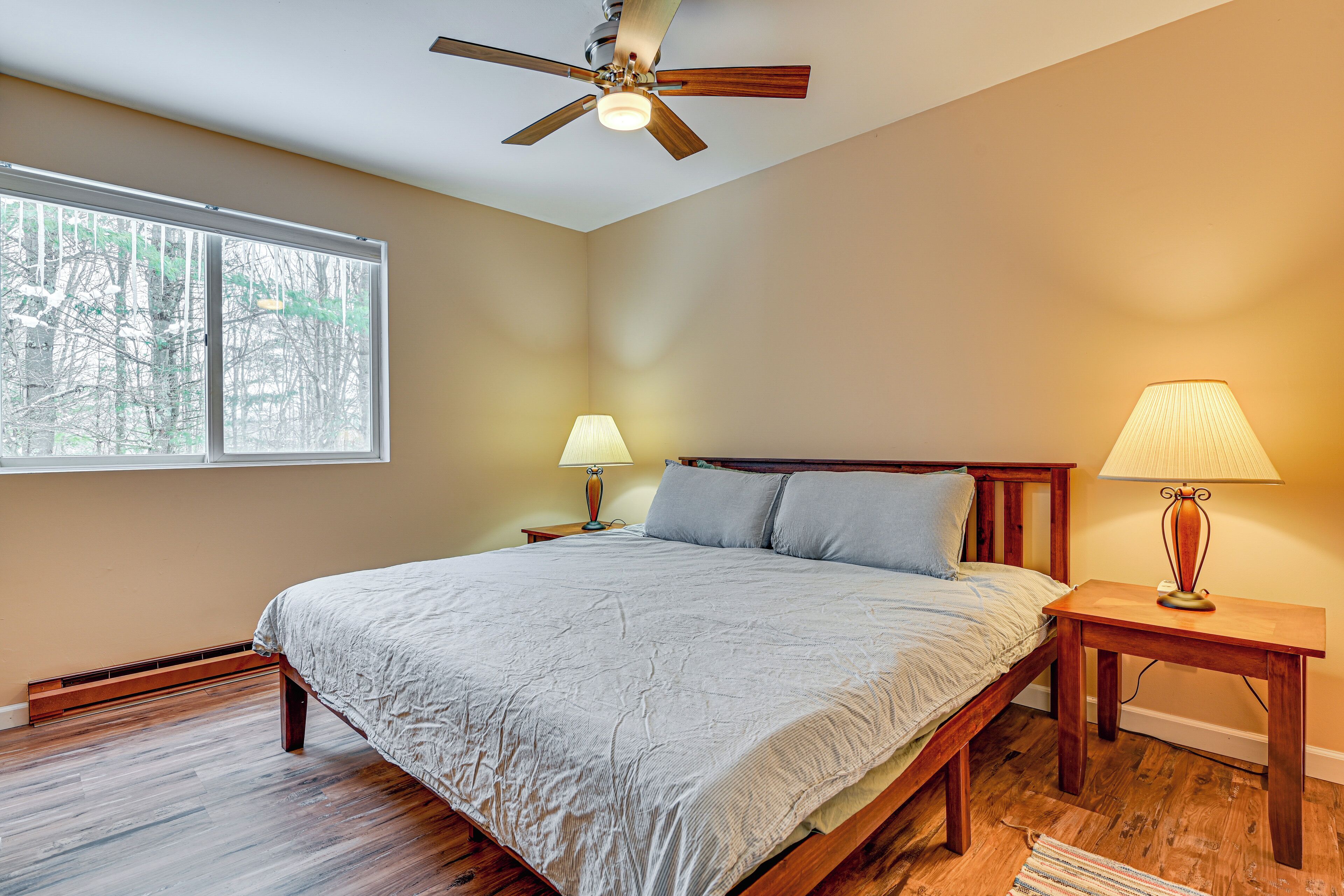 A bedroom with a bed, two bedside tables, a ceiling fan, and a window.