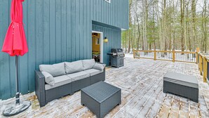 Eine überdachte Terrasse mit einem blauen Gebäude, einem grauen Sofa, einem roten Sonnenschirm und einem Grill.