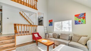 Ein geräumiger Wohnbereich mit einer Holztreppe, einem roten Sessel, einem beigen Sofa und einem Couchtisch.