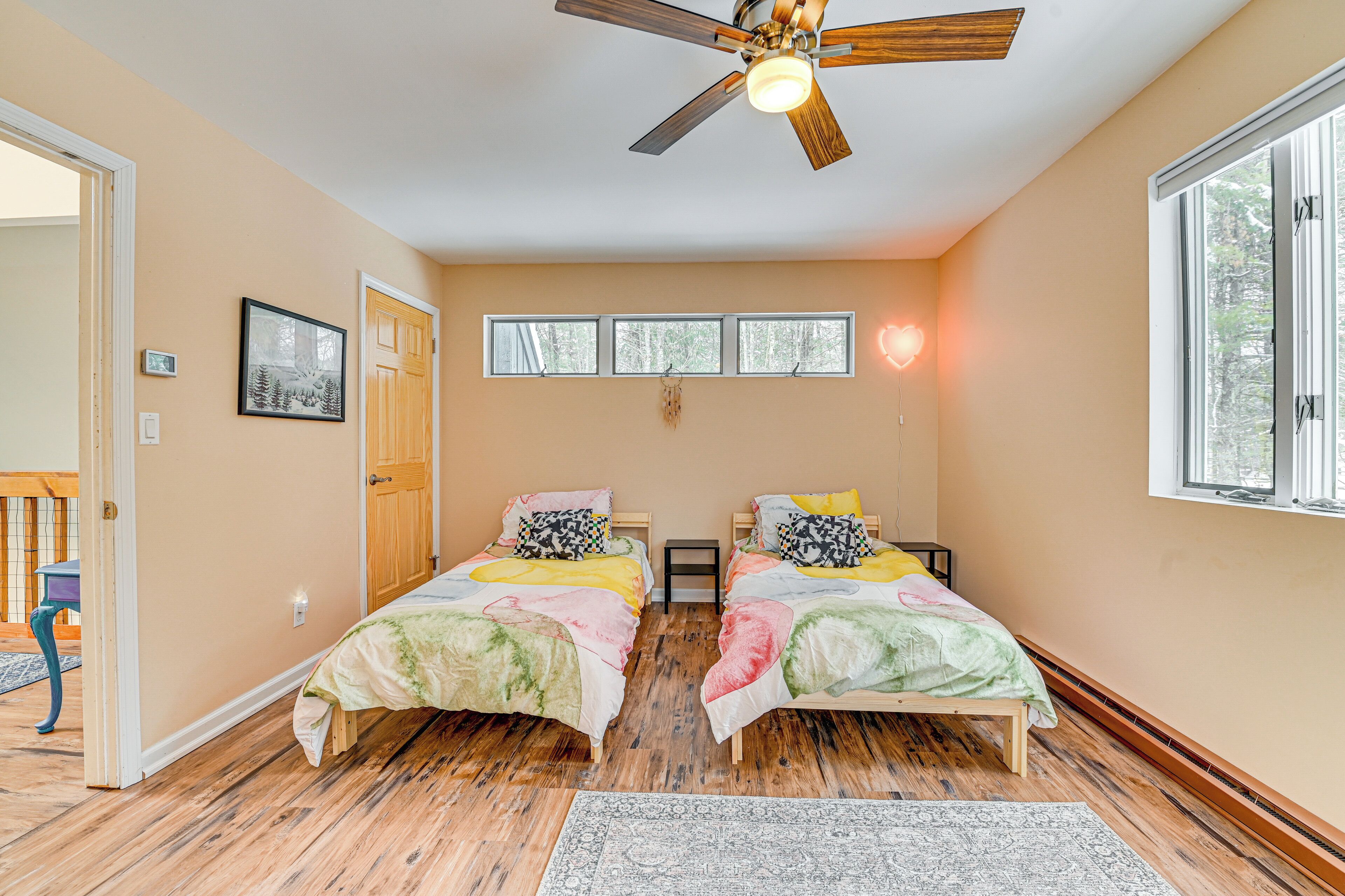 A bedroom with two beds, a ceiling fan, a window, and a door.