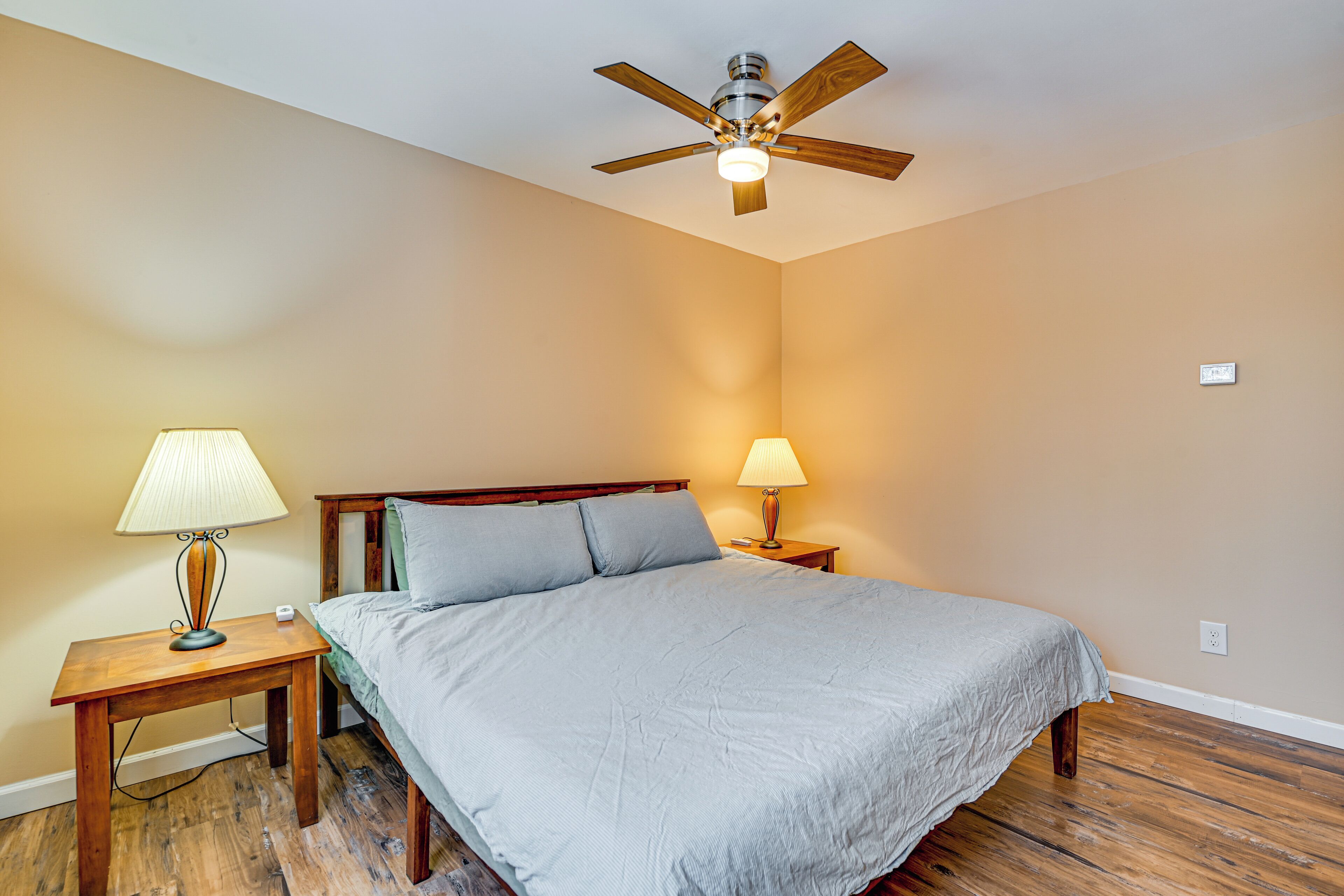Une chambre à coucher comprenant un lit, deux tables de chevet, un ventilateur de plafond et une prise électrique murale.