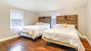 Un dormitorio con dos camas, cabeceros de madera, ropa de cama blanca y un ventanal grande.