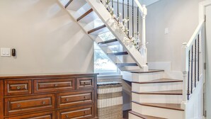 Una escalera con barandillas blancas y un pasamanos de madera que conduce a un rellano con una pared blanca y una ventana.
